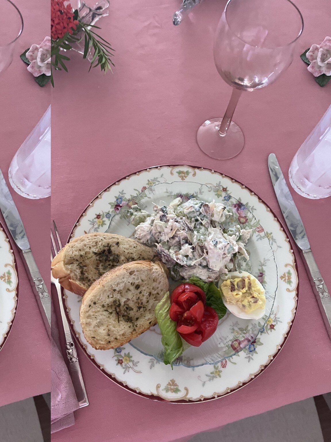 A plated meal on floral china against a pink tablecloth.